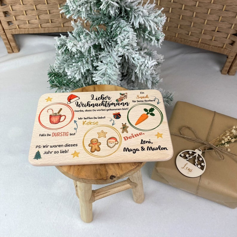 May include: A wooden Christmas sign with a red Santa hat, a mug of hot chocolate, a gingerbread man, a Santa Claus, a carrot, and the text "Lieber Weihnachtsmann Danke, dass Du vorbei gekommen bist! Wir hoffen Du Liebst Kekse Falls Du DURSTIG bist PS: Wir waren dieses Jahr so lieb! Deine, Leni, Maya & Marlon"