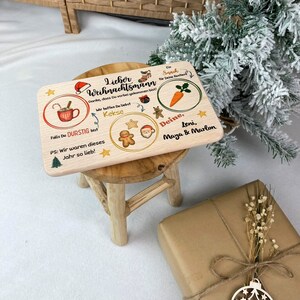 May include: A wooden sign with a Christmas theme. It says "Lieber Weihnachtsmann" and has illustrations of a cup of hot chocolate, gingerbread cookies, a carrot, and Santa Claus. The sign also says "Danke, dass Du vorbei gekommen bist!" and "Wir hoffen Du liebst Kekse".