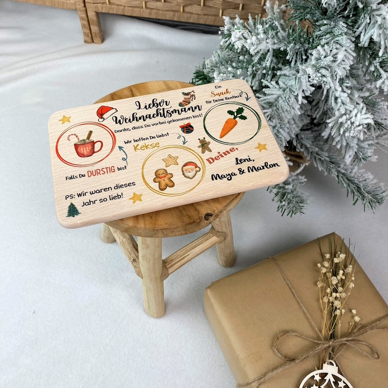 May include: A wooden sign with a Christmas theme. It says "Lieber Weihnachtsmann" and has illustrations of a cup of hot chocolate, gingerbread cookies, a carrot, and Santa Claus. The sign also says "Danke, dass Du vorbei gekommen bist!" and "Wir hoffen Du liebst Kekse".