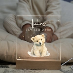 Könnte beinhalten: Personalisiertes Nachtlicht mit Holzsockel. Die transparente Acrylplatte zeigt eine Aquarellillustration eines Eisbärenbabys und den Namen "Lukas" mit Geburtsdaten: 13. Mai 2023, 18:43 Uhr, 50 cm und 3850g.