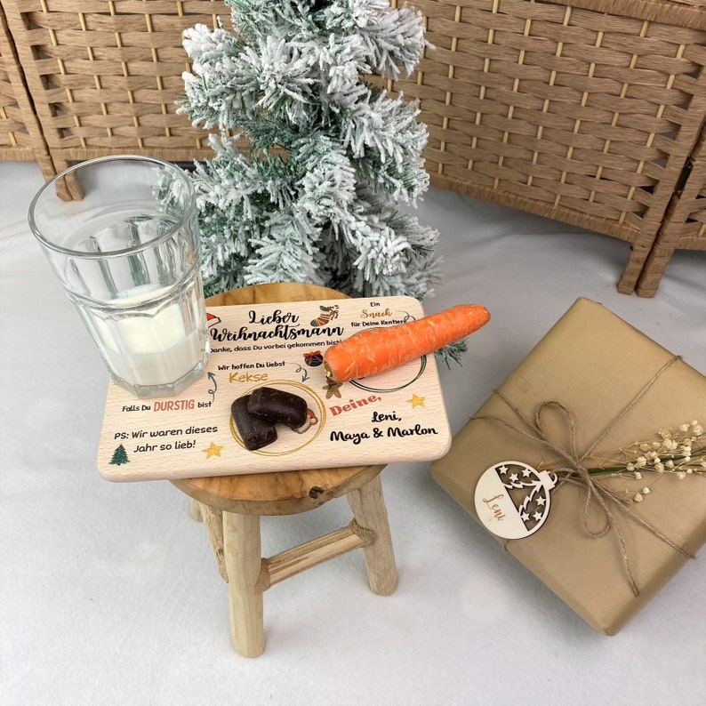 May include: A wooden Christmas plate with a carrot, two chocolate cookies, and a handwritten message that reads "Lieber Weihnachtsmann, Danke, dass Du vorbei gekommen bist. Wir hoffen Du liebst Kekse. Deine, Leni, Maya & Marlon. Falls Du durstig bist, PS: Wir waren dieses Jahr so lieb!"