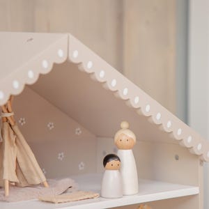 Puede incluir: Una casa de mu&ntilde;ecas de madera con un techo festoneado y lunares blancos. En el interior, hay un tipi en miniatura, una alfombra y dos mu&ntilde;ecos de madera. La casa de mu&ntilde;ecas est&aacute; pintada en tonos neutros.
