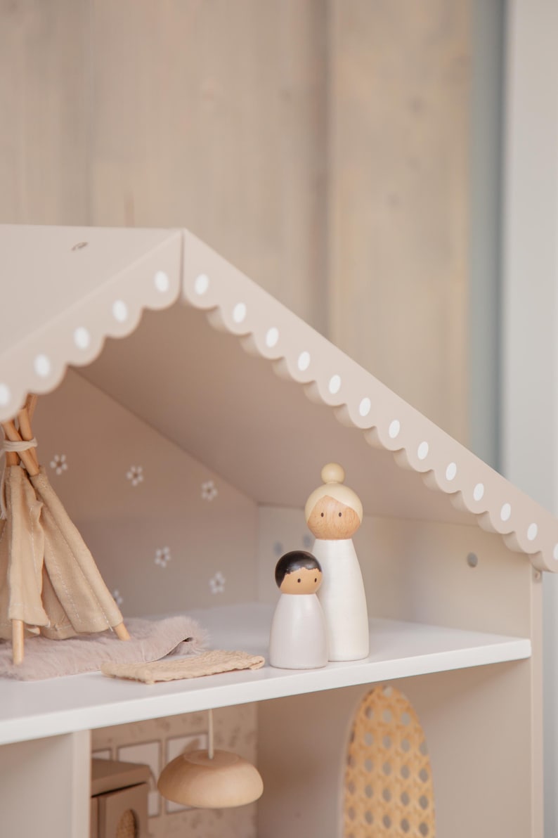 Puede incluir: Una casa de mu&ntilde;ecas de madera con un techo festoneado y lunares blancos. En el interior, hay un tipi en miniatura, una alfombra y dos mu&ntilde;ecos de madera. La casa de mu&ntilde;ecas est&aacute; pintada en tonos neutros.