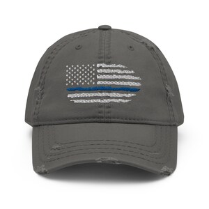 Può includere: Un berretto da baseball grigio consumato con una bandiera americana ricamata in bianco con una linea blu al centro.