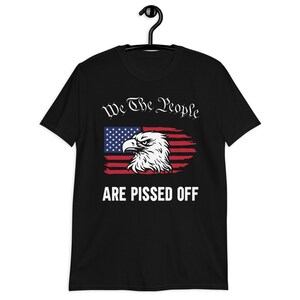 Pode incluir: Camiseta preta com um design de bandeira americana desbotada com uma &aacute;guia careca e o texto "We The People Are Pissed Off."