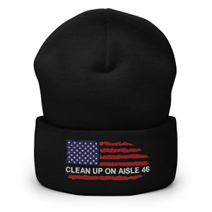 Puede incluir: Gorro negro con una bandera americana roja, blanca y azul y el texto "CLEAN UP ON AISLE 46" bordado en la parte delantera.