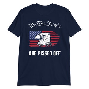 Pode incluir: Camiseta azul marinho com um design de bandeira americana desbotada e uma cabe&ccedil;a de &aacute;guia. O texto "We The People Are Pissed Off" &eacute; impresso em branco.