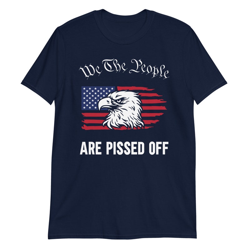 Pode incluir: Camiseta azul marinho com um design de bandeira americana desbotada e uma cabe&ccedil;a de &aacute;guia. O texto "We The People Are Pissed Off" &eacute; impresso em branco.