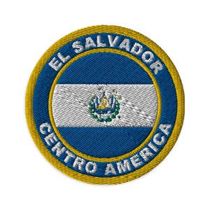 Può includere: Una toppa circolare ricamata con la bandiera di El Salvador al centro. La bandiera è blu e bianca con lo stemma nazionale al centro. Le parole "El Salvador" e "Centro America" sono ricamate attorno alla bandiera in un cerchio giallo.