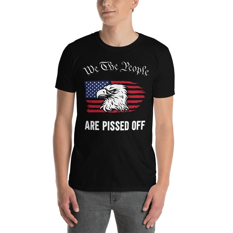 Pode incluir: Camiseta preta com um design de bandeira americana desbotada e o texto "We The People Are Pissed Off".