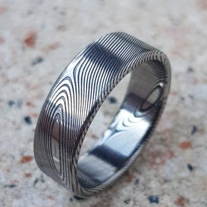 May include: A silver ring with a unique patterned design. The ring is made of metal and has a smooth, polished finish.