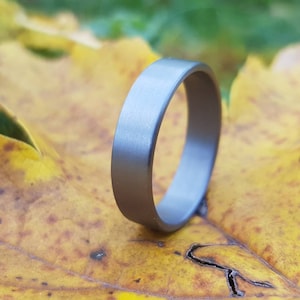 Könnte beinhalten: Ein einfacher, gebürsteter Silberring. Der Ring ist glatt und hat eine matte Oberfläche.