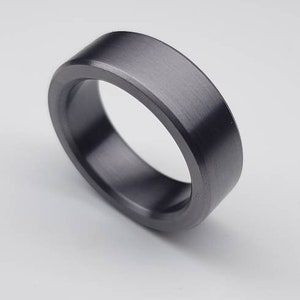May include: A dark gray brushed metal ring with a flat, wide band.