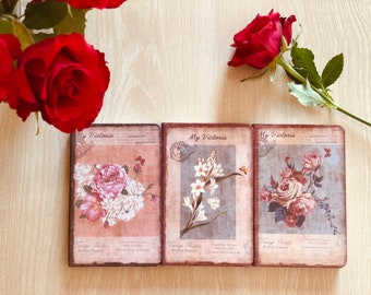 May include: Three vintage-style journals with floral designs. Each journal has a brown cover with the text "My Victoria" and "Vintage Recipes" printed on it. The journals feature different floral designs, including roses, lilies, and other flowers.