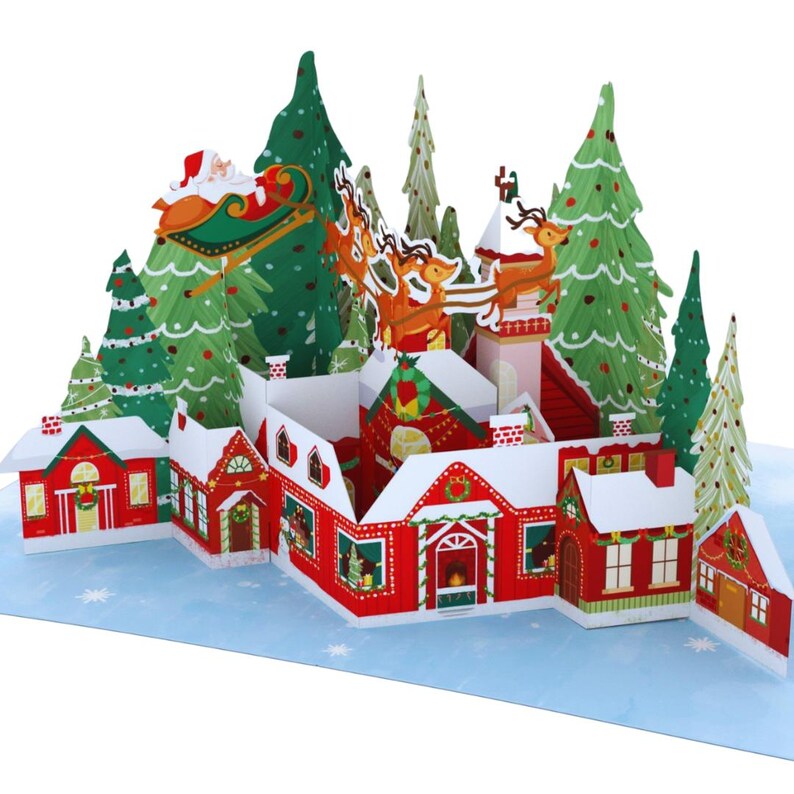 May include: A 3D pop-up Christmas card featuring a red and white village with Santa Claus flying over in a sleigh pulled by reindeer. The card is decorated with green trees and white snow.