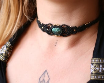 May include: A black macrame choker necklace with a green gemstone pendant. The necklace is worn by a person with long blonde hair.