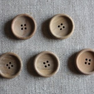 Könnte beinhalten: Sechs Holz-Knöpfe mit jeweils vier Löchern. Die Knöpfe sind hellbraun und haben eine glatte, leicht strukturierte Oberfläche.