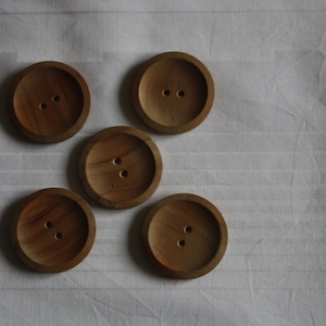 Op de afbeelding: Vijf houten knopen met elk twee gaten. De knopen zijn bruin en hebben een glad, afgerond oppervlak.