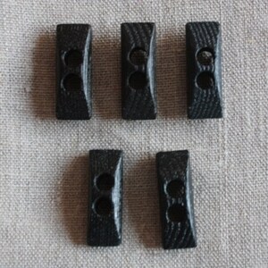 Könnte beinhalten: Fünf schwarze Holz-Toggle-Knöpfe mit jeweils zwei Löchern. Die Knöpfe sind in zwei Reihen angeordnet, mit drei Knöpfen in der oberen Reihe und zwei Knöpfen in der unteren Reihe.