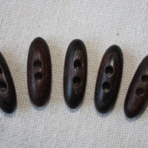 Könnte beinhalten: Sechs braune Holzknöpfe mit jeweils zwei Löchern. Die Knöpfe sind oval geformt und haben eine glatte Oberfläche.