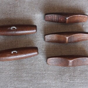 Könnte beinhalten: Sechs Holzstäbchen liegen auf einer hellbraunen Stoffoberfläche. Die Stäbchen sind braun und leicht gebogen.