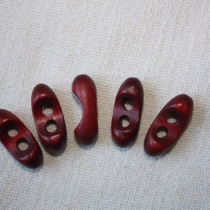 Peut inclure: Six boutons à bascule en bois de couleur rouge foncé. Les boutons sont de forme ovale avec deux trous chacun.