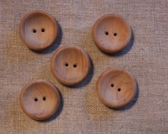 May include: Five round wooden buttons with two holes each, arranged on a textured, tan fabric. The buttons have a natural wood grain and a slightly concave design.