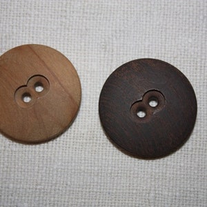Könnte beinhalten: Zwei runde Holz-Knöpfe mit jeweils zwei Löchern. Der Knopf links ist hellbraun und der Knopf rechts ist dunkelbraun.