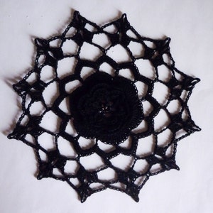 Könnte beinhalten: Schwarze Häkeldeckchen mit einem floralen Design in der Mitte.