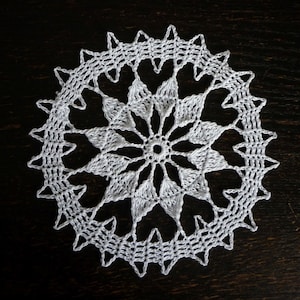 May include: White crocheted doily with a delicate floral design. The doily is circular and has a scalloped edge.