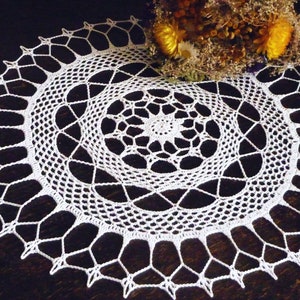 Puede incluir: Doily de ganchillo blanco con un diseño circular. El doily tiene un patrón delicado e intrincado con una estrella central.
