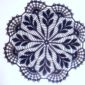 Può includere: Un centrino all'uncinetto nero con un delicato disegno floreale. Il centrino è circolare e ha un foro centrale.