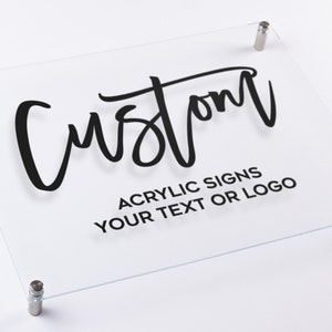 May include: A clear acrylic sign with the word "Custom" written in black script. The sign also includes the text "Acrylic Signs Your Text or Logo".