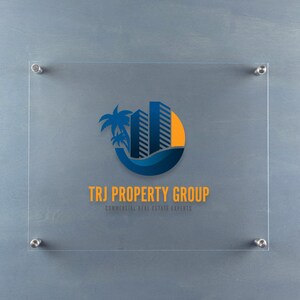 May include: A clear glass sign with a blue and yellow logo of a palm tree and buildings with the text "TRJ PROPERTY GROUP" and the tagline "COMMERCIAL REAL ESTATE EXPERTS".