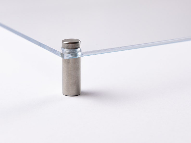 May include: A clear acrylic display stand with a silver metal stand. The stand is designed to hold a framed picture or other object.