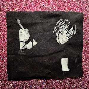 Op de afbeelding: Zwart-witte strijkpatch met een gestileerde illustratie van een persoon die een penseel vasthoudt en een gezicht.