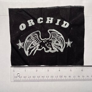 May include: Black fabric patch with a white winged panther and the word "ORCHID" in a white arc above the panther. Two white stars are on either side of the panther.