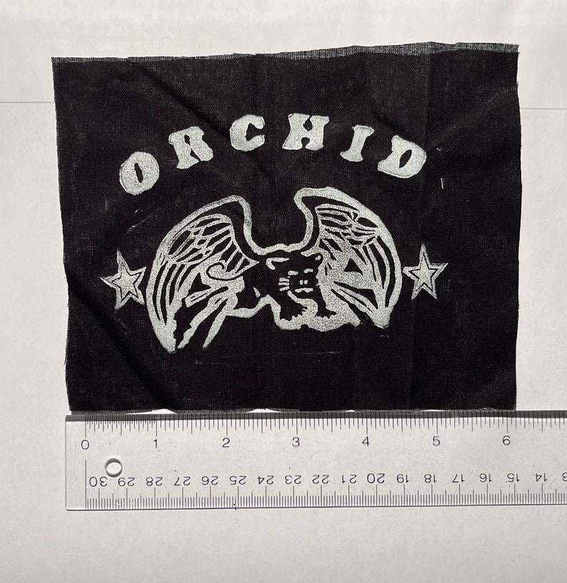 May include: Black fabric patch with a white winged panther and the word "ORCHID" in a white arc above the panther. Two white stars are on either side of the panther.