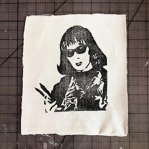May include: Black and white illustration of a person wearing sunglasses and a jacket. The person is holding a pair of scissors in their hand.