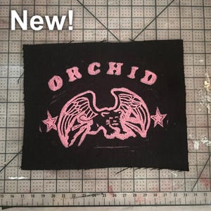 May include: A black fabric patch with pink lettering that reads "ORCHID" and a pink winged panther with stars on either side.