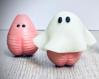 May include: Three small, pink, textured, ghost-shaped figures. One figure is wearing a white ghost costume.