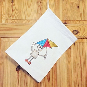 May include: A white canvas tote bag with a hand-drawn illustration of a robot holding a colorful umbrella. The robot is gray with red and yellow accents. The umbrella is blue, red, and yellow.