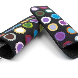 Könnte beinhalten: Zwei schwarze Stoff-Brillenetuis mit bunten Punkten. Ein Etui ist geöffnet und enthält eine Brille.