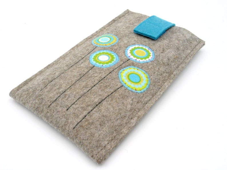 May include: A gray felt phone case with a blue leather flap closure. The case is decorated with colorful embroidered flowers.