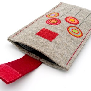 May include: A gray felt phone case with a red velcro closure and colorful embroidered flowers.