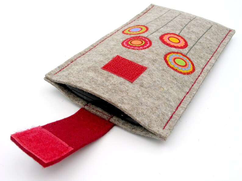 May include: A gray felt phone case with a red velcro closure and colorful embroidered flowers.