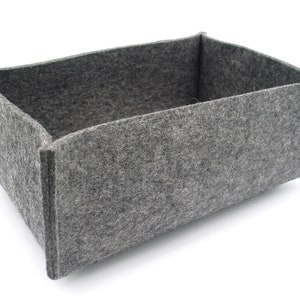 Könnte beinhalten: Eine graue Filz-Aufbewahrungsbox mit rechteckiger Form. Die Box ist leer und hat eine glatte, strukturierte Oberfläche.
