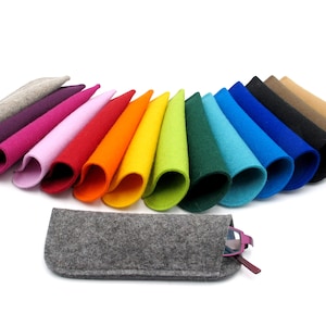 Könnte beinhalten: Ein Set mit 14 Filz-Brillenetuis in verschiedenen Farben, darunter Grau, Lila, Rosa, Rot, Orange, Gelb, Grün, Blau und Braun. Die Etuis sind in einem Halbkreis angeordnet, wobei ein graues Etui vorne liegt und eine Brille enthält.