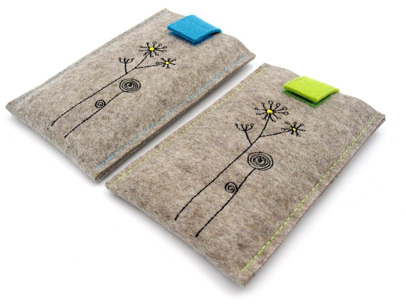 May include: Two gray felt phone cases with a simple black floral design and a contrasting colored flap closure. The case on the left has a blue flap and the case on the right has a green flap.