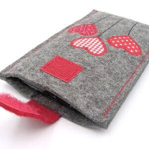 May include: A grey felt phone case with a red felt flap and three red felt hearts with white polka dots and gingham patterns.